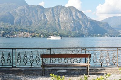 Bench by sea against mountains