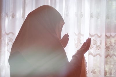 Rear view of woman standing by window at home