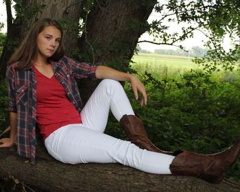 Young woman sitting on tree trunk in park