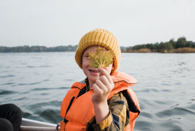Young boy on a fishing boat holding a maple leaf up looking happy