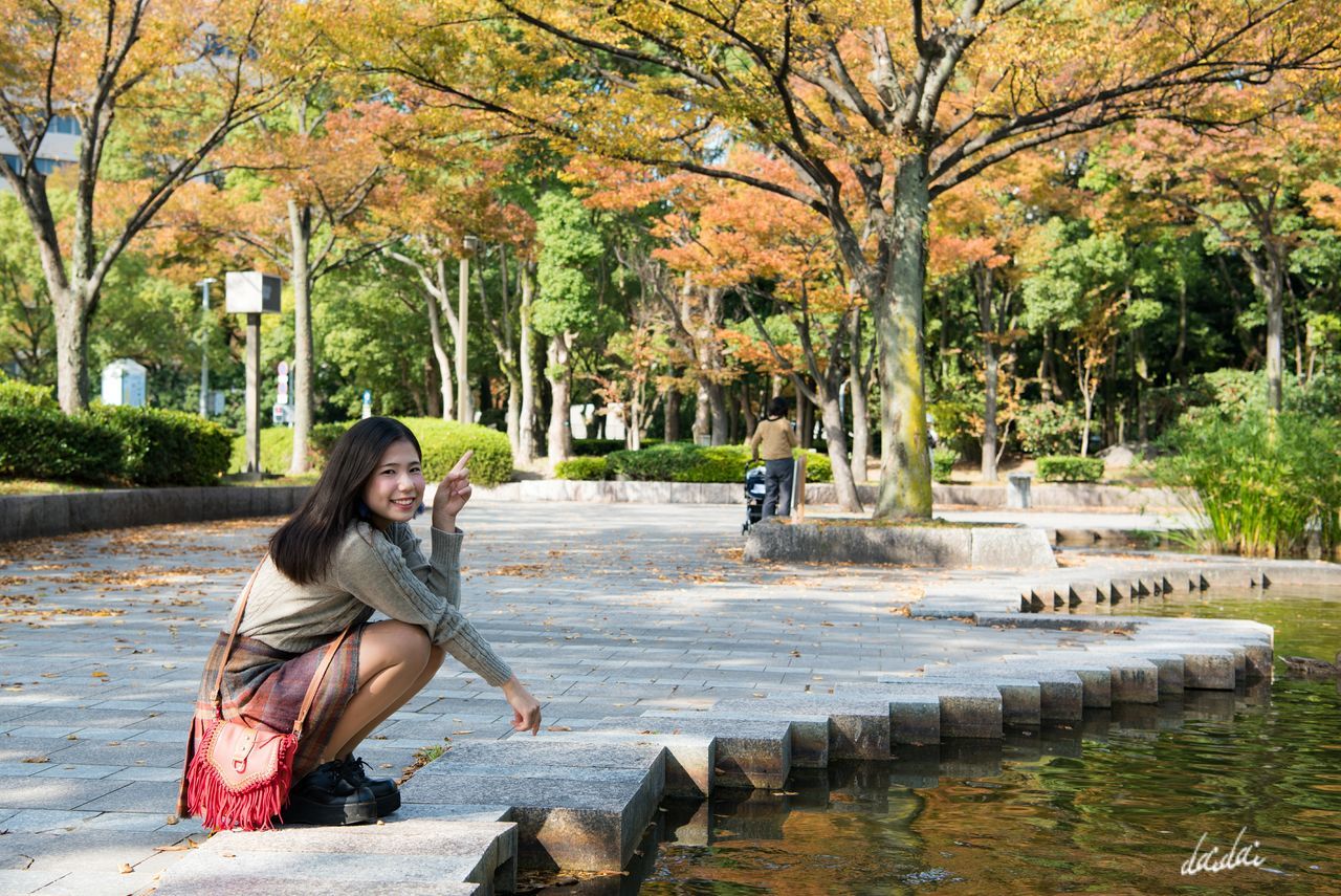 tree, water, outdoors, one person, full length, day, beautiful woman, leisure activity, real people, casual clothing, young adult, relaxation, lifestyles, young women, sitting, nature, smiling, beauty, building exterior, adults only, only women, one woman only, people, adult