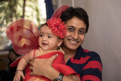 Portrait of happy man holding daughter wearing costume against wall