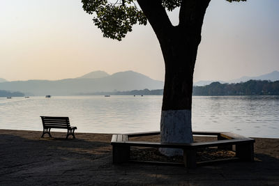 Bench by lake against sky