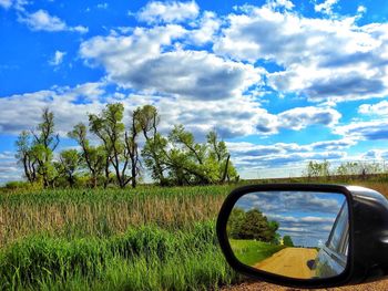 Reflection of side-view mirror on field against sky