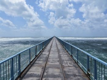 View of wooden bridge over sea against sky