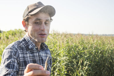 Man holding marijuana joint while standing on field against sky