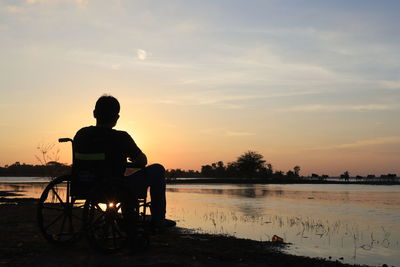 Rear view of silhouette man standing by lake against sky during sunset