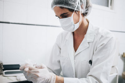 Doctor with a mask on her face and a plastic cap preparing gauze in a hospital operating room