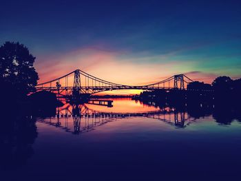 Silhouette bridge over river against sky at sunset