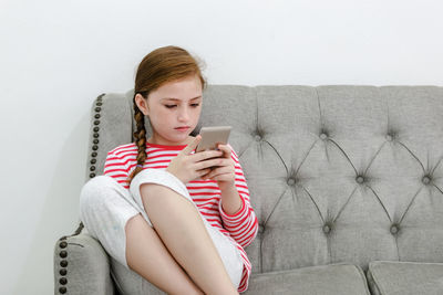 Teenage girl using mobile phone while sitting on sofa