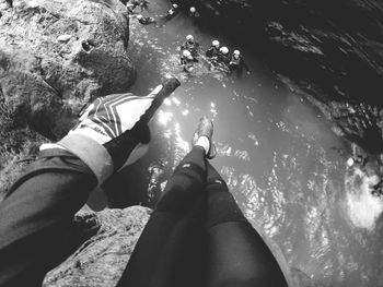 Low section of woman gesturing while sitting on rock over river