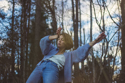 Young woman with short hair dancing against trees in forest