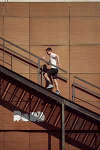 Side view of energetic male athlete running up metal staircase near building during training in summer