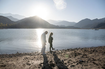 Senior man walking with his granddaughter along the lake shore with mountains.