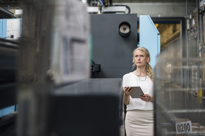 Woman with tablet at machine in factory shop floor looking around