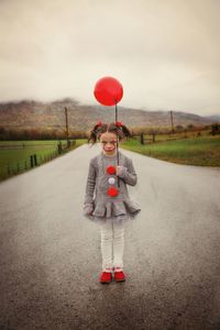 Rear view of girl standing on road at field against sky