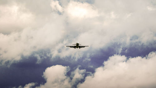 Low angle view of airplane flying in cloudy sky