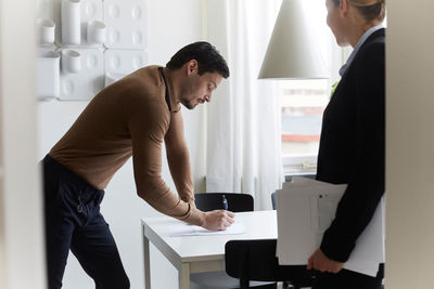 Mid adult man signing document while standing by real estate agent at new home