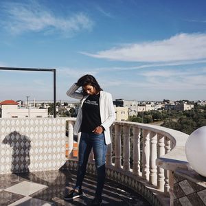 Full length of woman standing on railing against sky