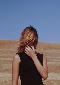 Woman covering face at beach against clear sky