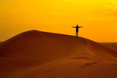 Silhouette man standing on desert against orange sky