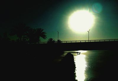 Silhouette trees by river against sky at night