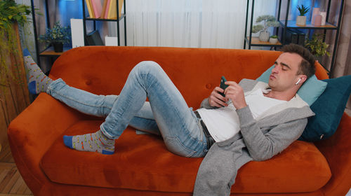 Young man lying on sofa and using smart phone