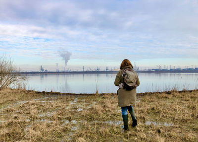 Rear view of woman standing on field looking at industry