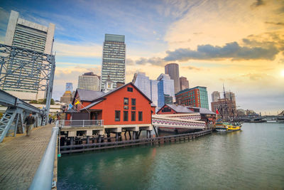 River by buildings in city against sky during sunset