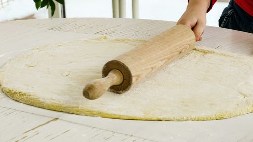 Cropped hand rolling pin on dough on table in kitchen