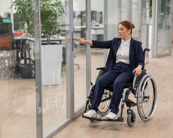 Red-haired caucasian woman in a wheelchair trying to open the door in the office