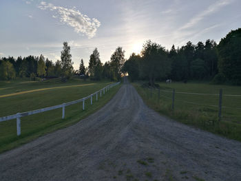 Dirt road amidst field against sky during sunset