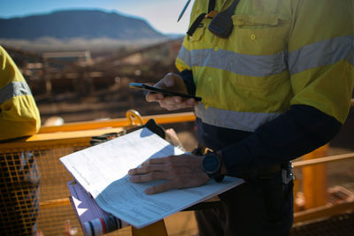 Midsection of worker using mobile phone at construction site