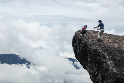 Low angle view of men standing on rock against sky