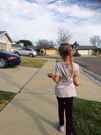 Rear view of girl holding cupcake while walking on sidewalk