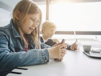 Siblings using smart phones sitting at table