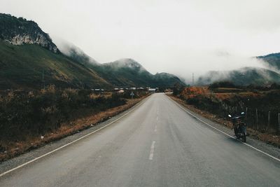 Road leading towards mountains during foggy weather