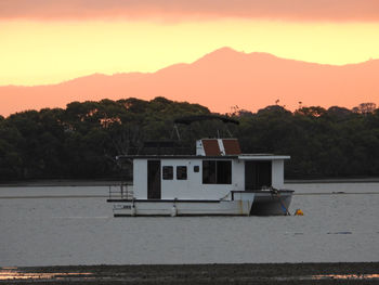 Built structure by lake against orange sky