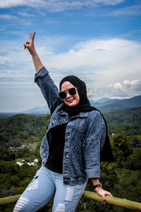 Young woman wearing sunglasses standing on mountain against sky