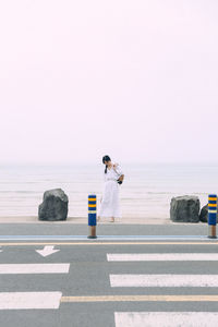 Woman on road by sea against sky