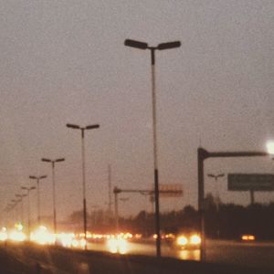 Illuminated street lights against sky at sunset