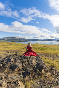 Woman sitting on landscape against sky