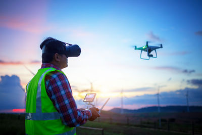 Engineer flying drone against sky during sunset