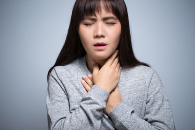 Beautiful young woman with neckache against gray background