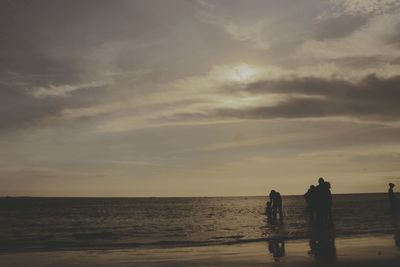 Silhouette people standing on shore against sea at beach