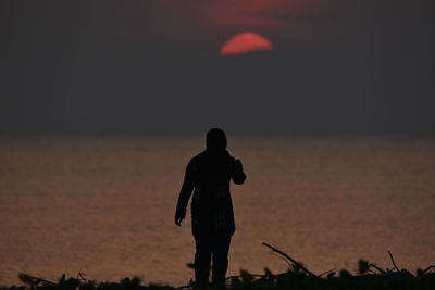 Rear view of silhouette man standing on beach during sunset