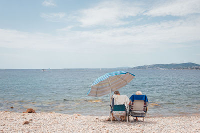 Rear view of couple sitting on beach against sky