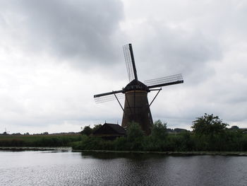 Traditional windmill by river against sky