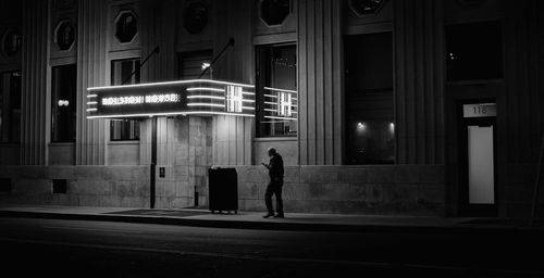 Rear view of woman walking on illuminated street at night