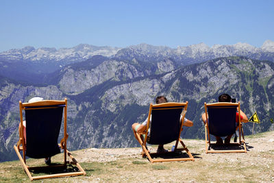 Chairs sitting on chair by mountains against clear sky